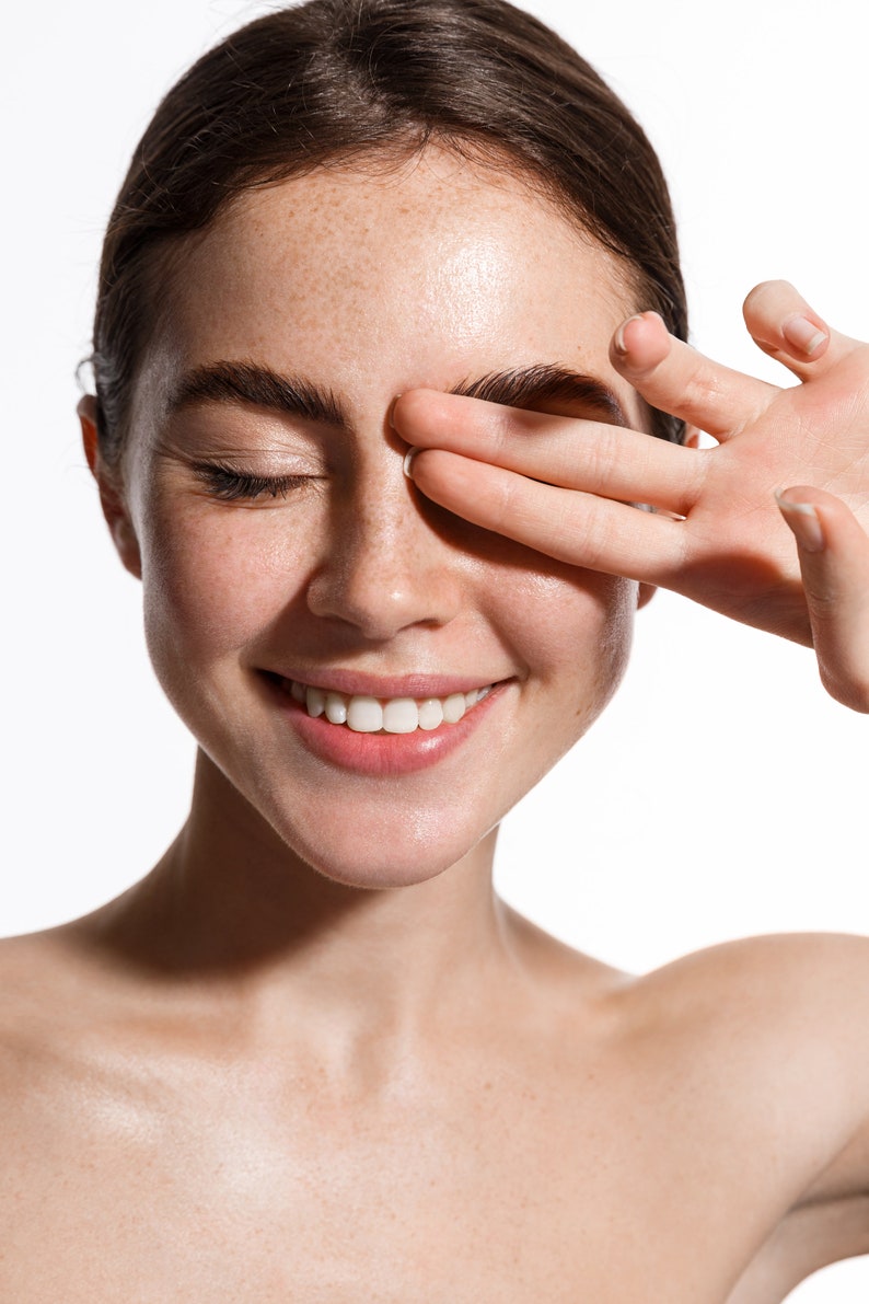 May include: A close-up of a woman's face with freckles, smiling with her eyes closed. Her hand is covering one eye.