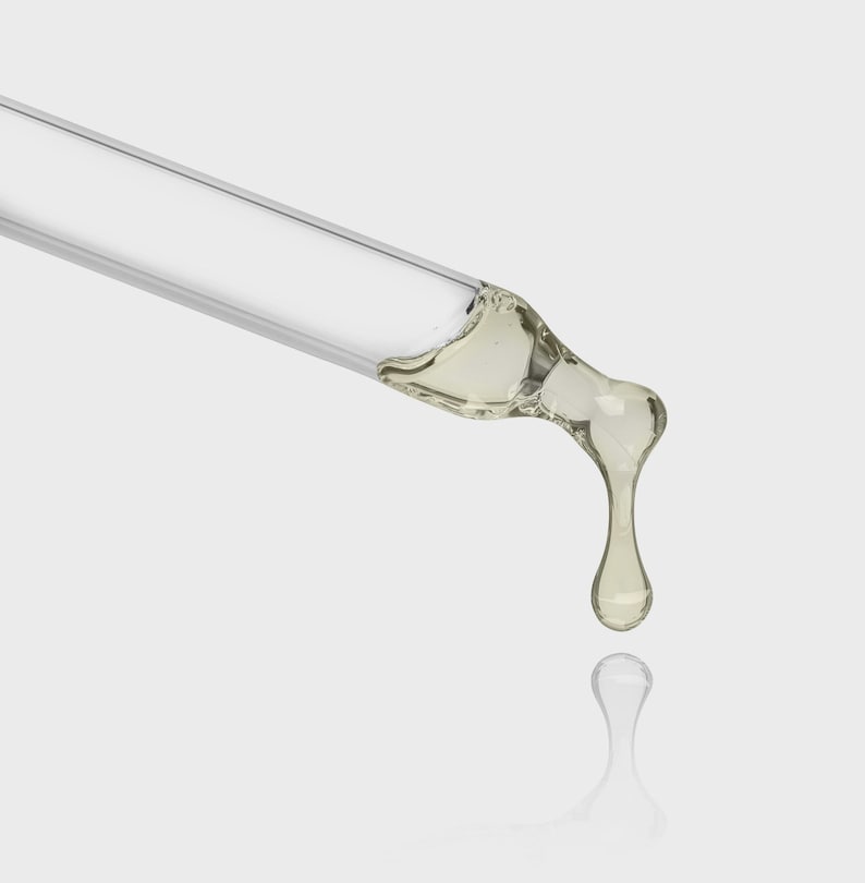 May include: A clear glass dropper with a light yellow liquid dripping from the tip. The dropper is angled diagonally across a white background, with a reflection of the droplet below.