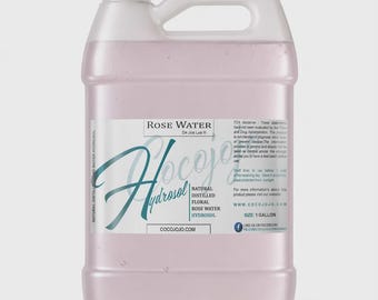 Puede incluir: Una garrafa de plástico translúcido de 1 galón llena de hidrosol de agua de rosas rosa pálido. La etiqueta blanca presenta el texto Rose Water, CocoJojo, Natural Distilled Floral Rose Water Hydrosol, indica un volumen de 1 galón y tiene tapa blanca.