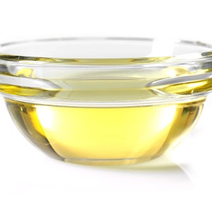 May include: A clear glass bowl filled with a golden yellow liquid, likely oil or vinegar, on a white background.