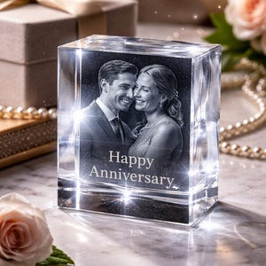 May include: A clear, rectangular crystal block featuring a laser-etched image of a smiling couple. The words "Happy Anniversary" are etched below the image. The block is surrounded by soft lighting and decorative elements.