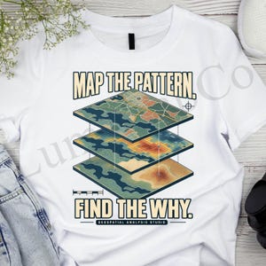May include: A white t-shirt featuring a graphic of three stacked, layered map segments. The text reads MAP THE PATTERN. FIND THE WHY. GEOSPATIAL ANALYSIS STUDIO. The design includes topographical lines, grid patterns, and a crosshair symbol.
