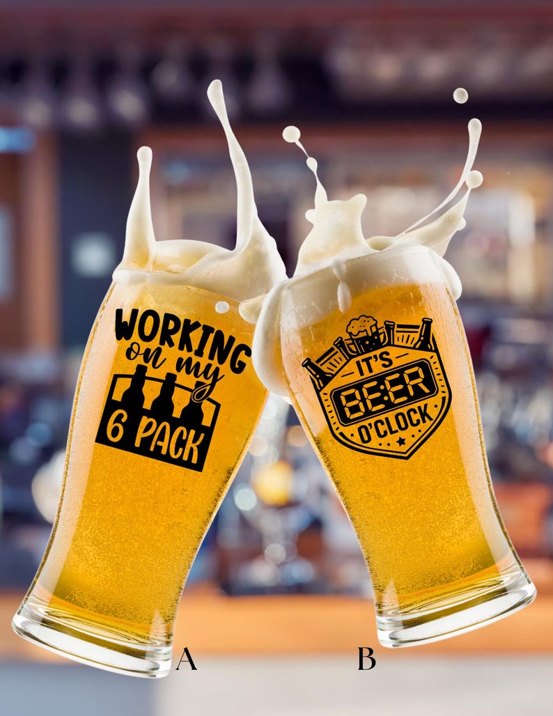 May include: Two clear glass beer glasses filled with golden lager, each featuring black printed text and graphics. The left glass displays 'WORKING on my 6 PACK' with bottle icons, while the right glass shows 'IT'S BEER O'CLOCK' with a beer mug icon.