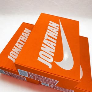 May include: Three orange boxes with the name "JONATHAN" in large white letters and a white Nike swoosh logo. The boxes have a label that reads "Jonathan's 8th Birthday April 30th, 2018".
