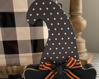 May include: Black and white polka dot witch hat with an orange ribbon and a black spider. The hat is made of wood and has a black brim.