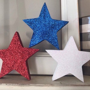 May include: Three glitter foam stars in red, white, and blue. The stars are a popular decoration for patriotic holidays.