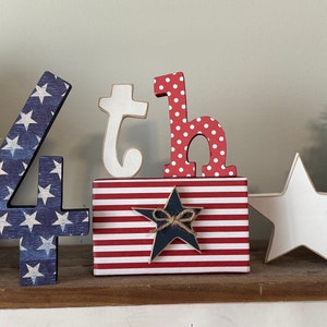 May include: Wooden 4th of July decorations with red, white, and blue stars and stripes. The numbers 4 and 'th' are decorated with an American flag pattern.