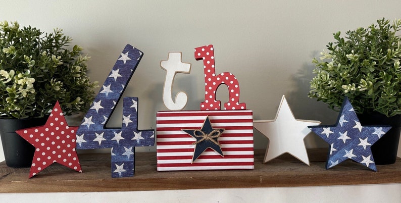 May include: Wooden 4th of July decorations with red, white, and blue stars and stripes. The numbers 4 and 'th' are decorated with an American flag pattern.