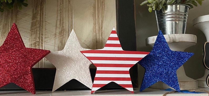 May include: Four decorative stars in red, white, and blue glitter. The stars are made of wood and have a 3D effect. They are perfect for adding a patriotic touch to your home decor.