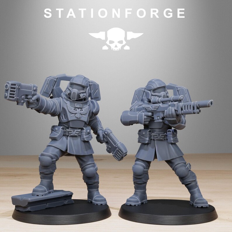 May include: Two grey unpainted miniature soldier figurines from StationForge. Each figure wears tactical armour with a chest eagle emblem, a helmet with a visor, and a backpack. One holds a pistol, the other a rifle. Both stand on black circular bases.