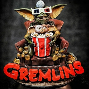 May include: A detailed sculpture of a Gremlin wearing 3D glasses, holding a popcorn bucket with a smaller Gremlin inside. The sculpture is seated in a red chair, with the word "GREMLINS" in red letters at the base. The sculpture is green, brown, and red.