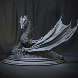 May include: A detailed, gray dragon sculpture with outstretched wings and a detailed head. The dragon is perched on a round base with a miniature castle scene. The sculpture is made of a textured material and is set against a dark background.