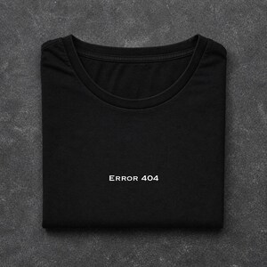 May include: A black short-sleeved t-shirt with a crew neckline. The centre of the chest features the white text "ERROR 404" printed in a clean, sans-serif font. The garment is folded neatly, displaying the front graphic and the collar detail.