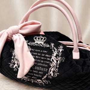 May include: A black quilted handbag featuring light pink handles and a large matching bow on the side. The front displays an embroidered crown and text that reads: Once upon a time a land far far away there were two set out to create the collection Couture the land and lived happily ever after.