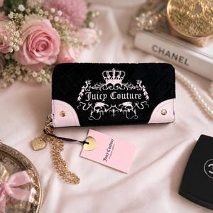 May include: Black quilted wallet with a crown and floral design, the words "Juicy Couture" are written in white. The wallet has pink accents and a gold chain. A pink tag with the words "Juicy Couture" is attached.