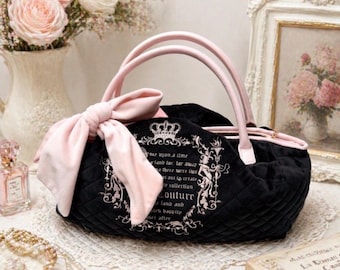 May include: A black quilted handbag featuring a large light pink bow on the side, light pink handles, and a zip closure. The front displays a white printed design with a crown icon and text that reads "once upon a time" and "Couture".