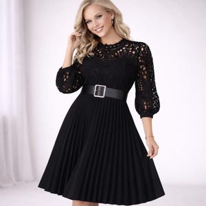 May include: Black dress featuring a lace bodice and pleated skirt. The dress has a high neckline, three-quarter sleeves, and a black belt with a silver buckle. The dress is knee-length and suitable for formal occasions.