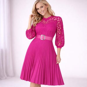 May include: A bright pink dress with a pleated skirt and a fitted bodice. The dress features a lace overlay on the sleeves and neckline, and a matching belt with a silver buckle. The dress is a vibrant color and has a classic, feminine silhouette.