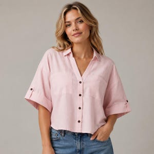 May include: A light pink button-down shirt with short sleeves and two front pockets. The shirt has a V-neck and dark brown buttons. The sleeves are rolled up, and the shirt is paired with blue jeans.