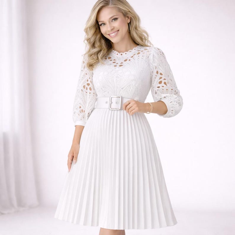 May include: A white dress with a pleated skirt and a white belt. The dress features a lace bodice and sleeves. The sleeves are three-quarter length. The dress has a round neckline. The belt has a silver buckle.