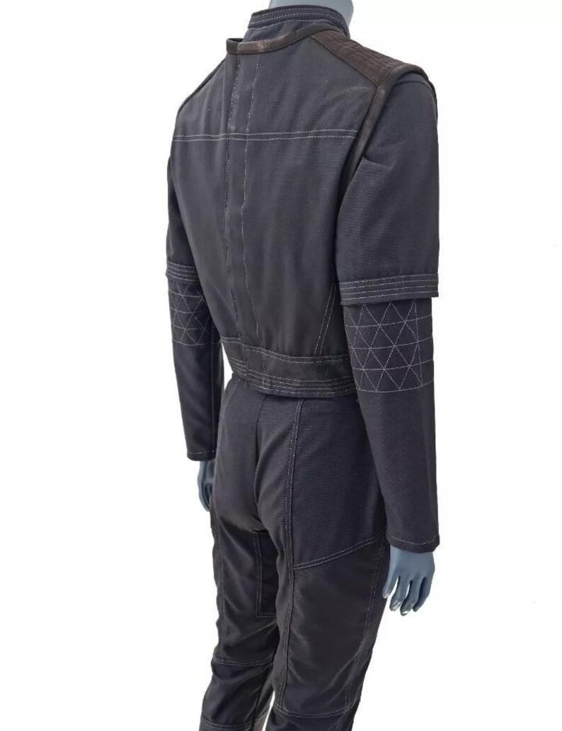 Op de afbeelding: Een donker antracietgrijze jumpsuit met een hoge kraag, lange mouwen met doorgestikte driehoekspatronen op de onderarmen en zichtbare lichtgrijze stiksels. Het kledingstuk heeft een gestructureerd lijfje en een nauwsluitende broek.