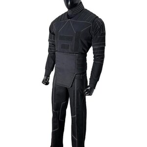 May include: A black long-sleeved shirt and matching trousers set featuring a high neck collar, structured chest panel, and reinforced waist section. The garment is detailed with white contrast stitching forming geometric patterns across the fabric.