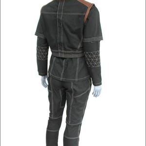 May include: A black two-piece outfit consisting of a jacket and pants with prominent white contrast stitching. The jacket features brown shoulder panels and a geometric triangular pattern on the sleeves. The pants have a matching seam design.