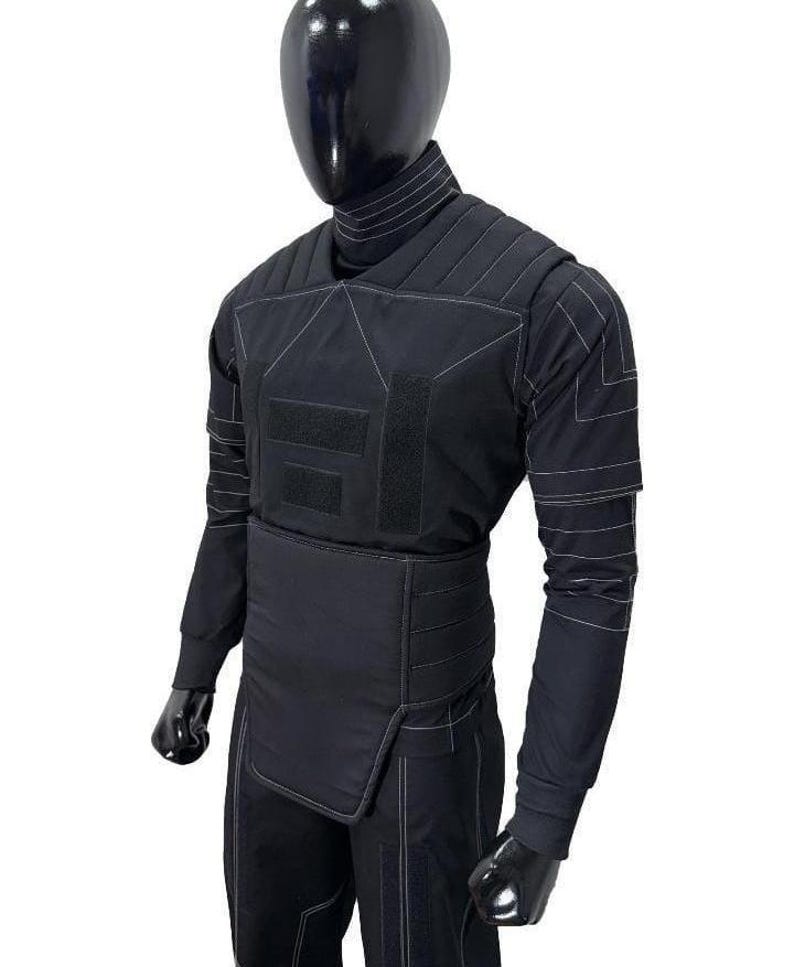 May include: A black long-sleeved tactical shirt featuring a high turtleneck collar, padded chest and shoulder panels, and a wide integrated waist belt. The garment is accented with white contrast stitching throughout and rectangular hook-and-loop patches.