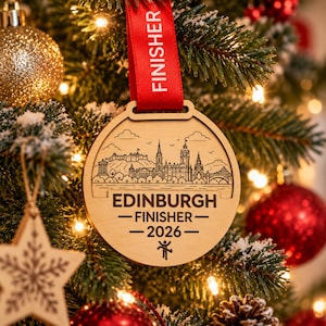 May include: A round wooden ornament featuring a laser-engraved skyline of Edinburgh, Scotland. The text reads EDINBURGH FINISHER 2026 with a small stick figure icon. A bright red ribbon with the word FINISHER printed in white is attached to the top.