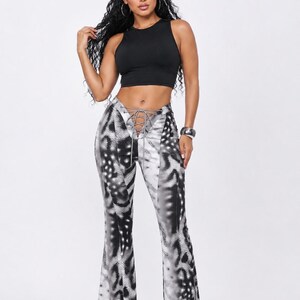 May include: A black sleeveless crop top paired with high-waisted flared pants featuring a black and white animal print pattern. The pants include a lace-up detail at the center front waist with thin matching ties and a fitted silhouette.