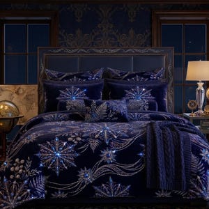 May include: A deep navy blue bedding set featuring a repeating pattern of silver and white snowflakes and fern leaves. The set includes a plush comforter, matching pillow shams, and a small rectangular accent pillow, all with a soft velvet texture.