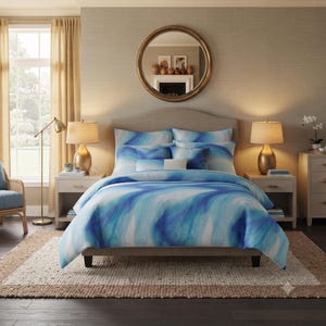 May include: A bedding set featuring a duvet cover and matching pillow shams with a fluid, abstract watercolour pattern in shades of deep blue, light blue, and white. The bedding is draped over a bed with a neutral-toned upholstered headboard.