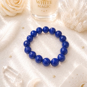 May include: A circular bracelet composed of faceted, deep blue spherical beads. The beads are uniform in size and arranged in a continuous loop, reflecting light across their polished surfaces. The bracelet is presented as a single, cohesive piece.