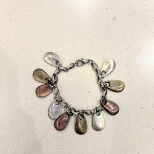 May include: A silver charm bracelet featuring teardrop-shaped charms in silver, copper, and gold hues. The bracelet has a chain link design and a clasp closure. The charms are evenly spaced around the bracelet.
