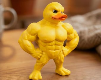 May include: A yellow duck figurine with a highly muscular, human-like physique. The duck has a bright orange beak, defined chest and abdominal muscles, and thick arms with hands on its hips. It stands in an upright, confident pose.