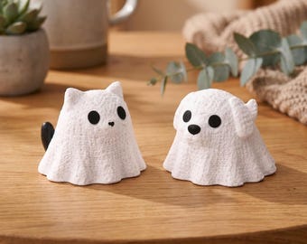 May include: Two white ceramic figurines, one shaped like a cat with a black tail and the other like a dog. Both have black eyes and noses. The figurines are on a wooden surface.