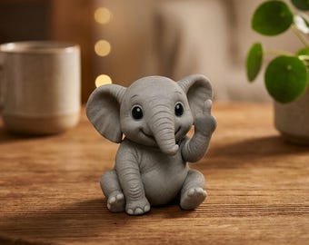 May include: A gray, smiling elephant figurine with large ears and a raised trunk. The elephant is sitting on a wooden surface. The figurine has large, dark eyes and is holding up its trunk.