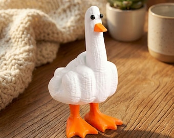 May include: A white goose figurine with orange feet and beak, and black eyes. The goose is standing on a wooden surface. The figurine has a textured surface and is a decorative item.