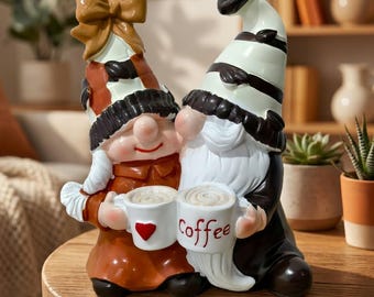 May include: A ceramic figurine of two gnomes holding coffee mugs. The gnomes wear hats with black and white stripes and brown and orange outfits. One mug has a red heart, and the other says "Coffee" in red.