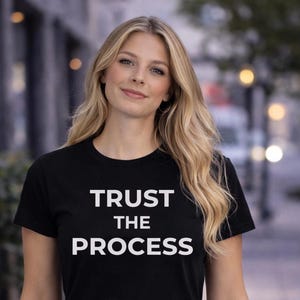 May include: Black crew neck t-shirt with the white text "TRUST THE PROCESS". The shirt is made of a soft material and is suitable for everyday wear. The t-shirt is a great gift idea.
