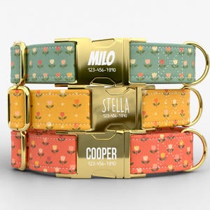 Puede incluir: Tres collares personalizados para perros apilados. Cada collar tiene una hebilla dorada con un nombre y un número de teléfono. Los collares tienen un estampado de pequeñas flores en tonos naranja, amarillo y rosa sobre fondos verdes, amarillos y naranjas.