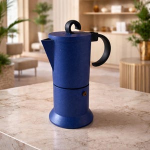 May include: A blue stovetop espresso maker with a black handle and lid handle. The coffee pot is cylindrical with a spout and a small brass-coloured knob. The surface has a speckled texture, and it sits on a light-coloured countertop.
