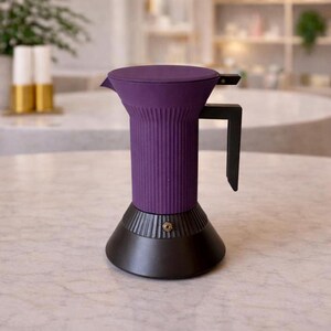 Può includere: Una moderna caffettiera viola e nera da piano cottura. La caffettiera ha un corpo cilindrico a coste, un manico nero e una base nera. Anche il coperchio è viola. La caffettiera è appoggiata su una superficie di marmo.