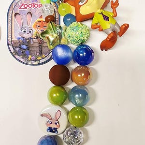 Op de afbeelding: Een Zootopia-sleutelhanger met een metalen sluiting, een ronde bedel met Judy Hopps en Nick Wilde, een Nick Wilde-figuurtje en twee strengen veelkleurige kralen, waaronder groene, blauwe, bruine en iriserende bollen met een Judy Hopps-kraal.