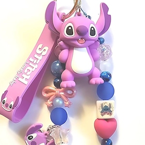 May include: A pink Stitch keychain with a gold-colored ring. The keychain features a Stitch figure, a pink strap with "Stitch lovely baby" text, and decorative beads in pink, blue, and white. A pink bow and a heart-shaped bead are also included.