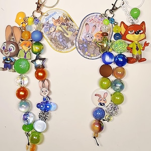 Op de afbeelding: Twee Zootopia-sleutelhangers met kralen en bedels van Judy Hopps en Nick Wilde. De sleutelhangers bevatten kleurrijke acryl- en parelkralen, stervormige accenten en ovale labels met Zootopia-afbeeldingen en de tekst Zootopia.
