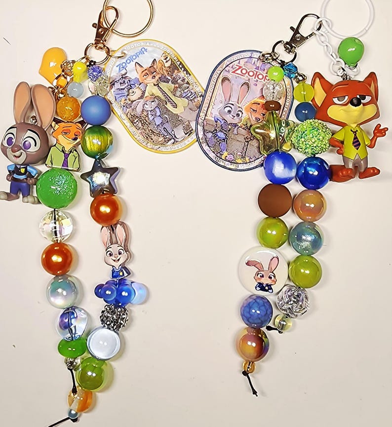 Op de afbeelding: Twee Zootopia-sleutelhangers met kralen en bedels van Judy Hopps en Nick Wilde. De sleutelhangers bevatten kleurrijke acryl- en parelkralen, stervormige accenten en ovale labels met Zootopia-afbeeldingen en de tekst Zootopia.