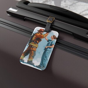 Puede incluir: Etiqueta de equipaje con una ilustración en acuarela de un bombero y una enfermera. El bombero viste uniforme y casco naranja, la enfermera, uniforme azul. La etiqueta está sujeta a un asa de maleta negra con una hebilla dorada.