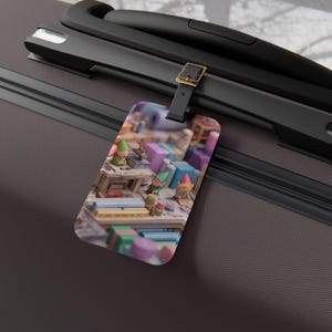 May include: A luggage tag featuring a whimsical scene of gnomes at work. The tag shows gnomes with green hats and red hats, working at a table surrounded by colorful blocks and tools. The tag is attached to a black suitcase.