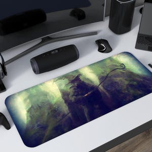 May include: A rectangular mouse mat with a green and blue abstract design, featuring a curved line. The mat is surrounded by black tech accessories, including a speaker, headphones, and a gaming controller. A laptop and mouse are also present.